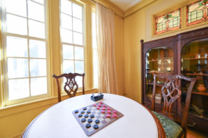 antique table, chairs, curio cabinet and windows with a checkers game waiting to be played